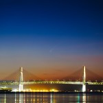 2024年秋、早朝の横浜の空に「紫金山・アトラス彗星」が姿を現した瞬間を、横浜ベイブリッジとともに捉えた一枚です。
明け方、太陽が昇る直前の空は夜の名残と朝の気配が交じり合い、深い青から淡いオレンジへと移ろう美しいグラデーションを描いています。その静かな空の中、横浜ベイブリッジの上空に、淡く伸びる彗星の姿が薄っすらと写り込み、はかなくも印象的な光景を生み出しています。
都会の象徴である橋と、遥かな宇宙から訪れた彗星が同じフレームに収まった、秋の明け方ならではの幻想的なコラボレーションです。