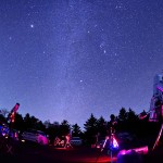 伊豆天城高原で撮影した1枚です。オリオン座のベテルギウス、こいぬ座のプロキオン、おおいぬ座のシリウス、の3つの一等星の中を冬の天の川が縦に流れています。夏の天の川と違ってとても淡いですが、冬の澄んだ夜空の中でくっきり見ることができました。左上にあるひときわ明るい星は木星です。
この日は前日まで降っていた雨が上がって、多くの天文ファンがここに集まっていました。彼らの望遠鏡が揃って空を見上げる様子を、星の宴と表現してみました。